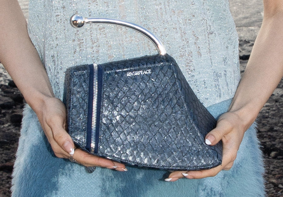 Person holding a black quilted handbag with 'Riverpeace' branding.