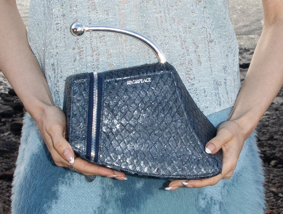 Person holding a black quilted handbag with 'Riverpeace' branding.