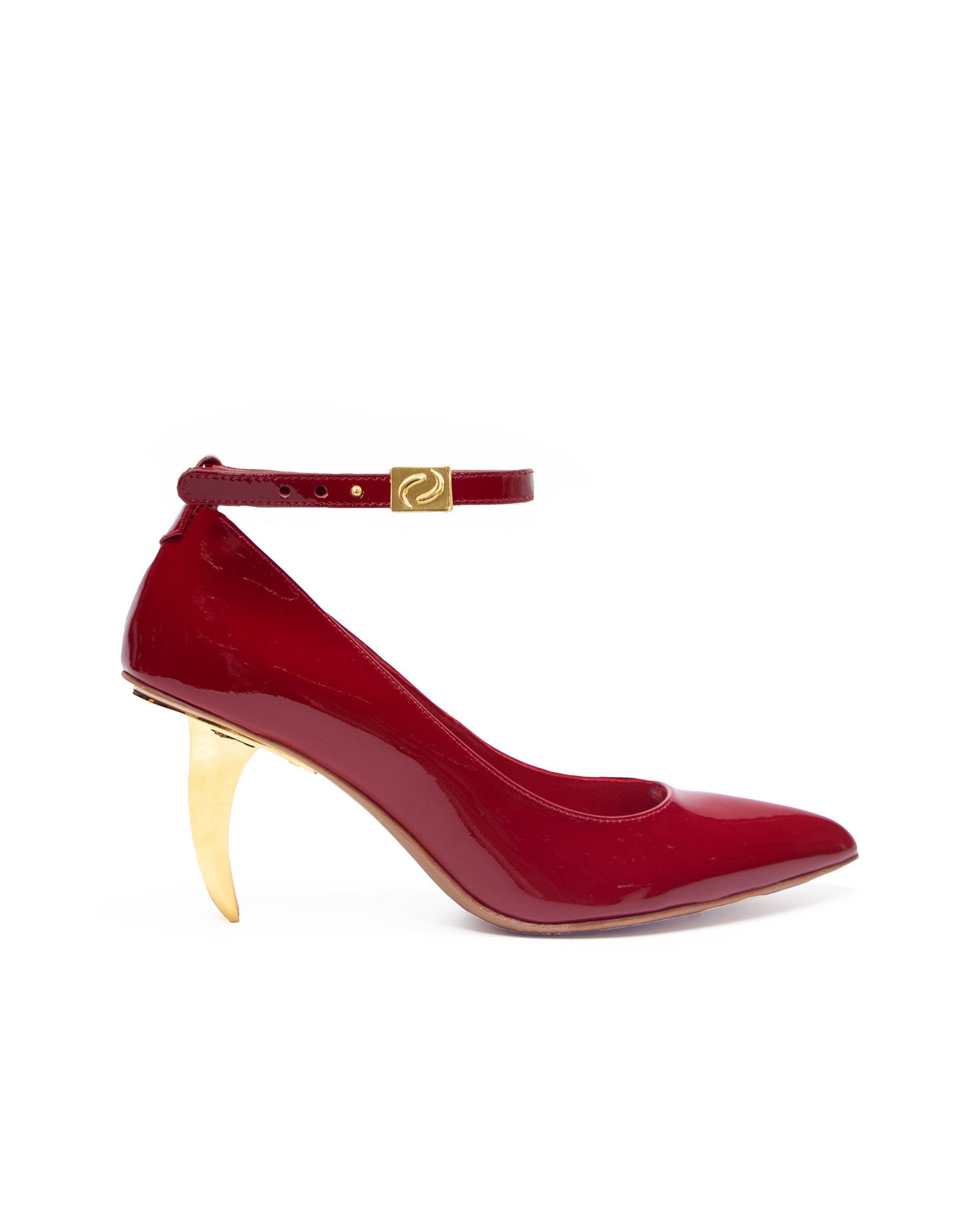 A red pointed-toe high heel shoe with a unique blade design heel and a logo at the ankle strap.
